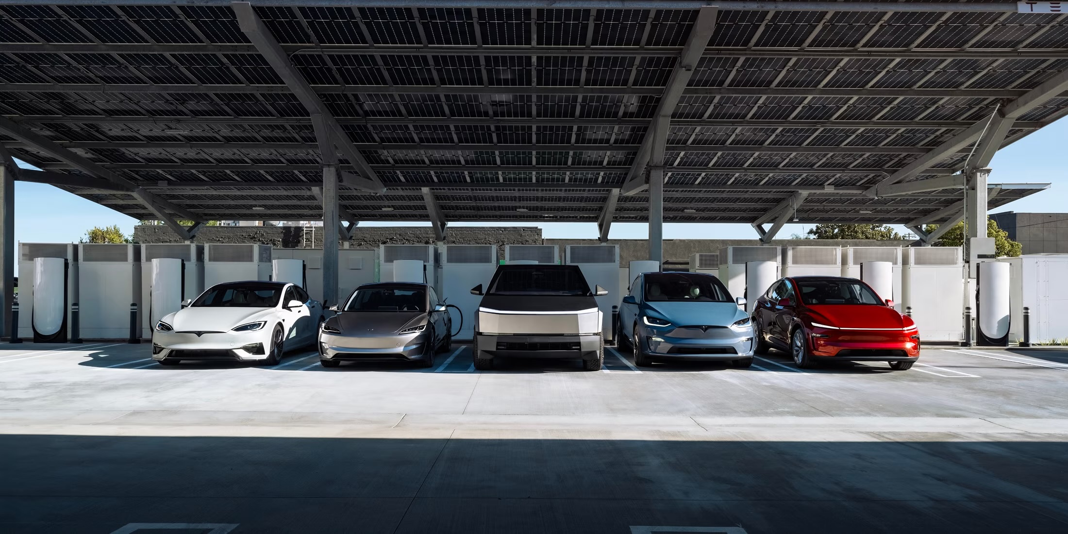 A Tesla Supercharger site under a solar canopy, five electric vehicles charging